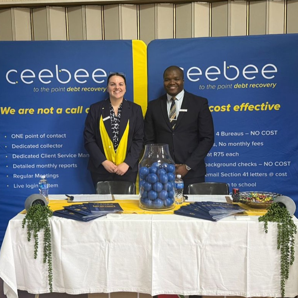 Two event staff in suits stand behind a promotional table for Ceebee debt recovery at a booth, with blue banners and a glass jar of blue balls in the center.