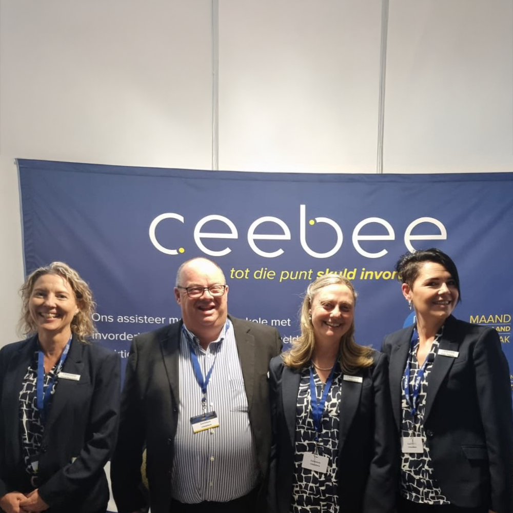 Four professionals pose for a group photo in front of a blue Ceebee banner at a conference or event, all wearing blazer and badges.