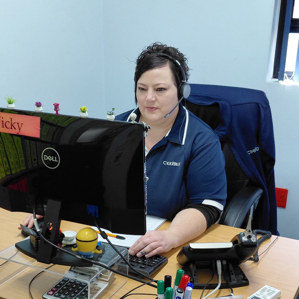 Woman with headset at a desk in an office, looking at a Dell monitor while typing on a keyboard at her workstation.
