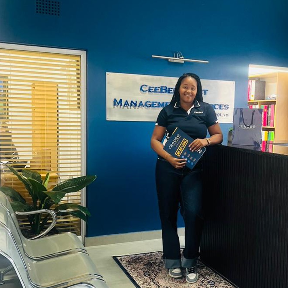 Woman standing in a blue-walled reception area, holding a blue brochure in front of a sign that says 'Management Services'
